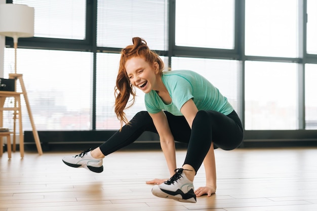 Радостная сильная молодая женщина в спортивной одежде делает сложную позу йоги дома на фоне окна Счастливая спортивная женщина делает упражнения йоги для силы тела
