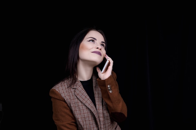 Joyful and successful young woman fashion blogger is emotionally talking on phone Beautiful young woman in casual grey jacket is holding smartphone