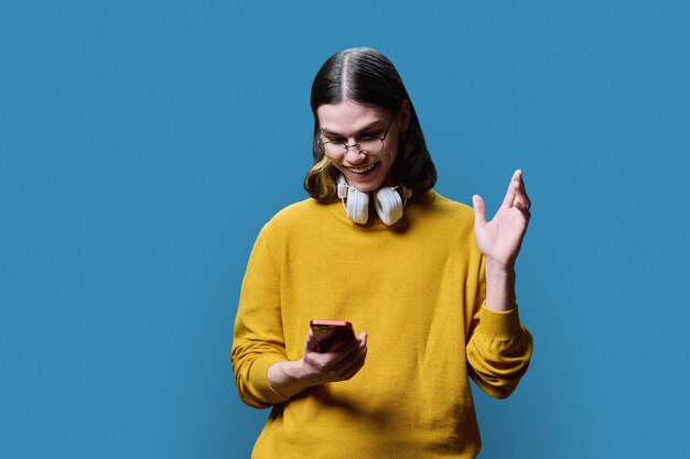 Joyful surprised young male looking in smartphone on blue background