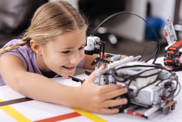 Foto gioioso giocattolo tecnologico. felice ragazza felice ispirata seduta nel laboratorio di robotica e guardando il cyber robot mentre esprime positività