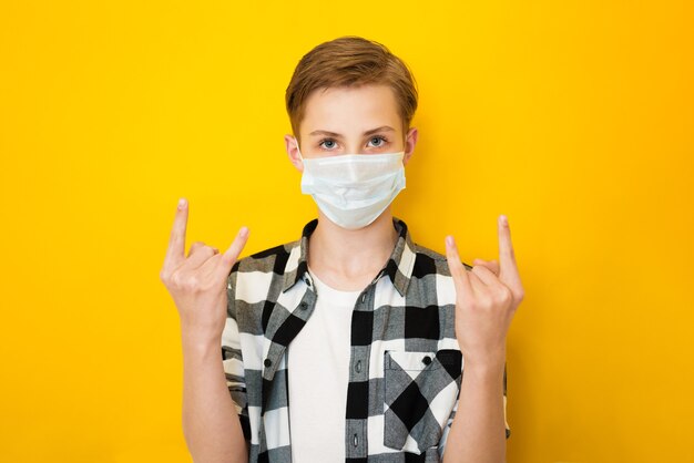 Joyful teen boy in fashionable clothes showing with raised arms horns or rock gesture