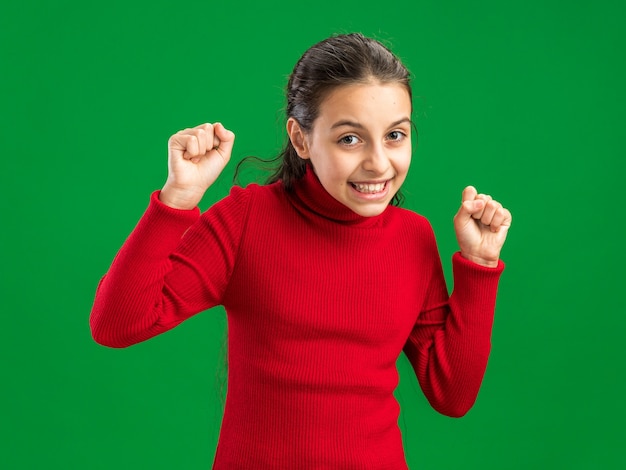 Joyful teenage girl looking at front doing yes gesture isolated on green wall