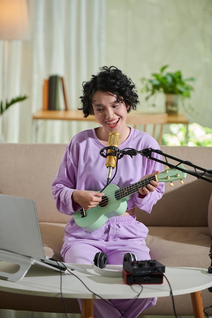 Joyful teenage girl recording herself playing ukulele and singing