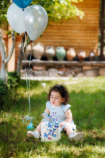 Foto una bambina gioiosa seduta sull'erba accanto ai palloncini e soffiando candele sulla torta di compleanno