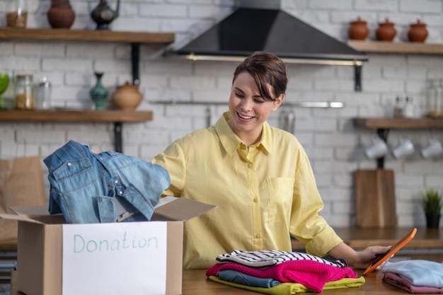 Joyful vlogger packing clothes for donation before the
camera