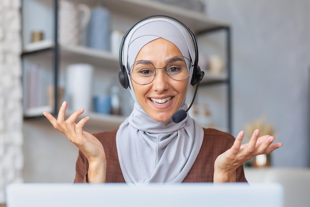 Donna allegra in hijab che lavora da casa in remoto donna musulmana che parla durante una videochiamata utilizzando l'auricolare