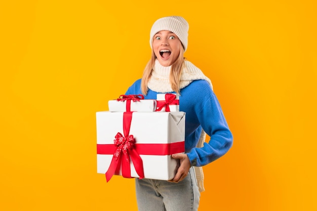 Joyful woman holding christmas boxes in a yellow studio exuding excitement and festive spirit