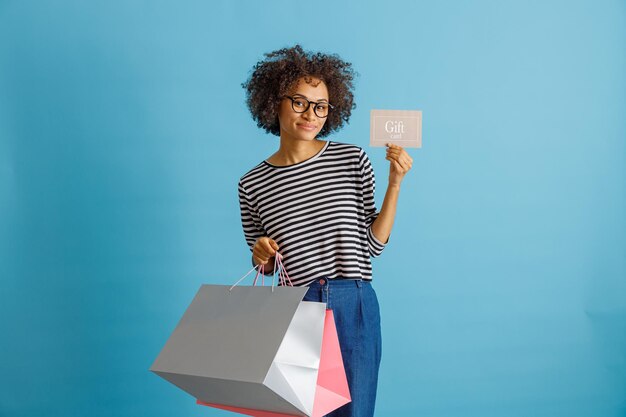 Joyful woman holding purchases and gift card