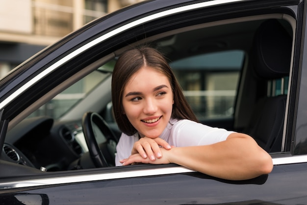 Joyful woman leaning her elbow over car window while enjoying road trip