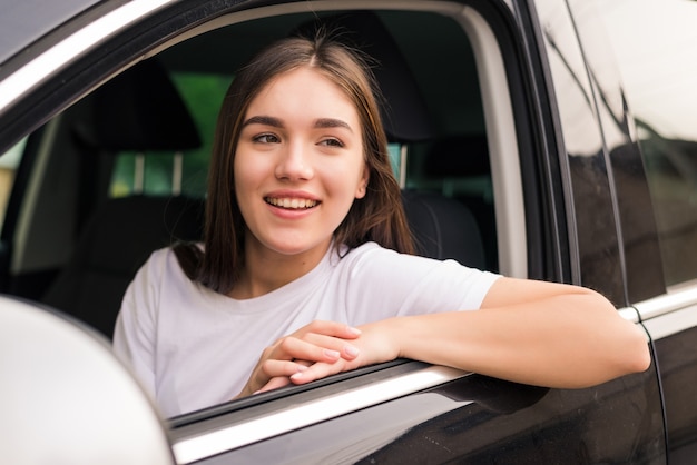 Joyful woman leaning her elbow over car window while enjoying road trip