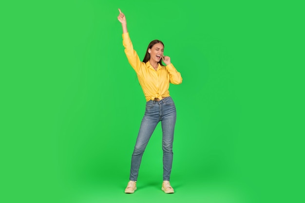 Joyful woman listening music singing song wearing earbuds green background