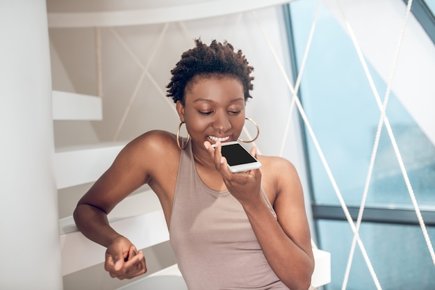 Joyful woman making voice message on smartphone