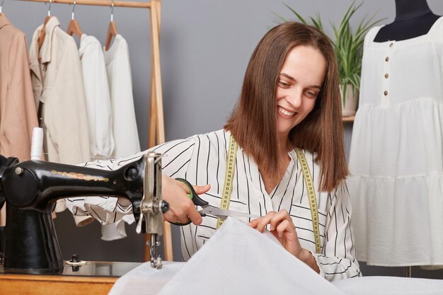 Joyful woman seamstress cutting textile in sewing studio workplace of sewer dressmaker cuts dress detail smiling happily designer creating new collection