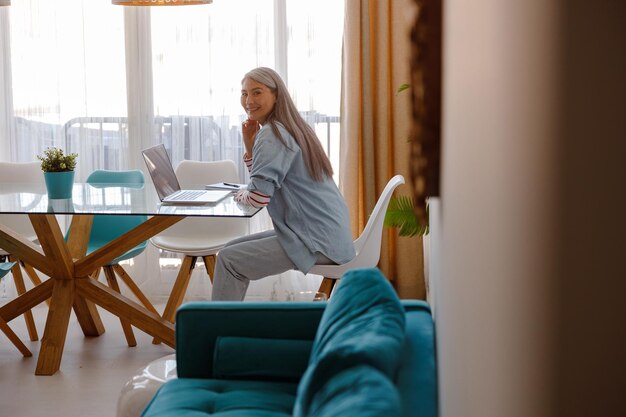 Радостная женщина сидит за столом с ноутбуком дома