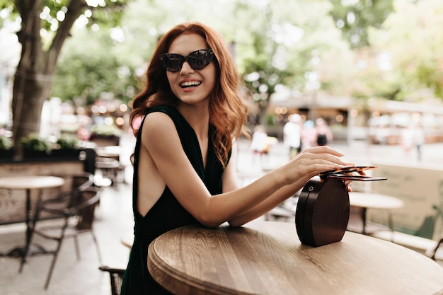 Joyful woman in sunglasses laughing and resting in street cafe