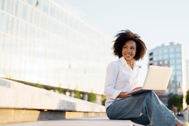 Радостная женщина, использующая ноутбук на открытом воздухе, представляющая удаленную работу и свободу в городской среде