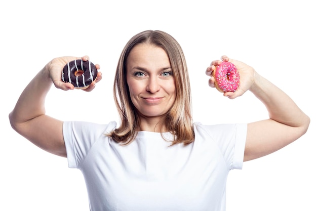 텍스트를 위한 흰색 배경 공간에 격리된 그녀의 손에 건강과 맛있는 정크 푸드를 입힌 도넛을 들고 흰색 티셔츠를 입은 즐거운 여성
