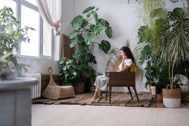 Joyful woman with laptop on knees in harmony with plants around feeling relax comfort at cozy home