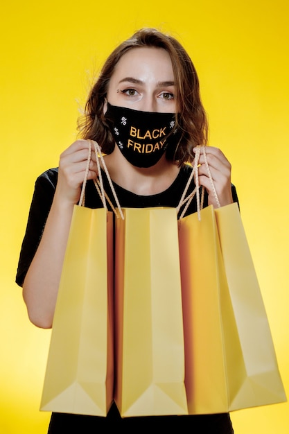 黄色の背景、ショッピング旅行のパッケージを持つうれしそうな女性。スタジオポートレート。ブラックフライデーセール。