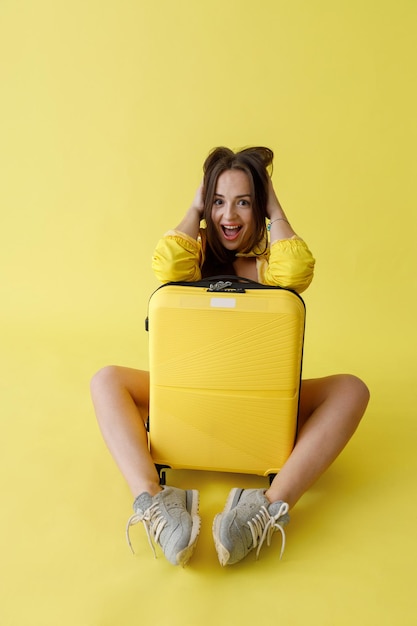 Joyful woman with trolley luggage bag posing in studio