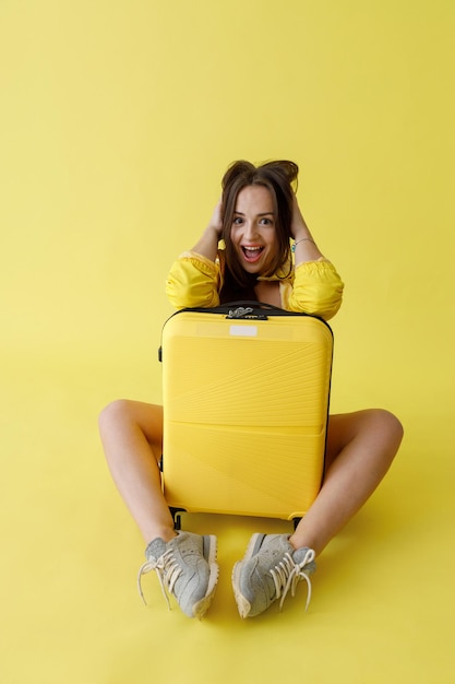 Donna allegra con la borsa dei bagagli del carrello che posa nello studio