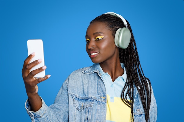 Joyful young african woman using smartphone and headphones