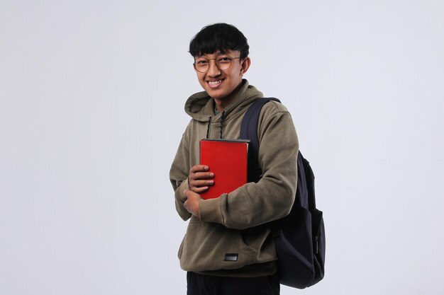 Gioioso giovane studente universitario asiatico in piedi mentre tiene in mano un libro