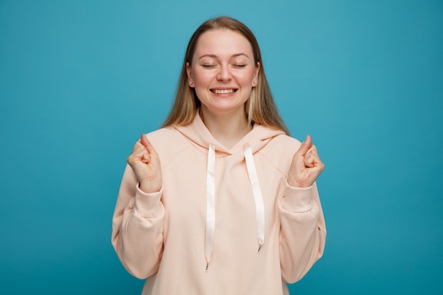 目を閉じてはいジェスチャーをしているうれしそうな若いブロンドの女性