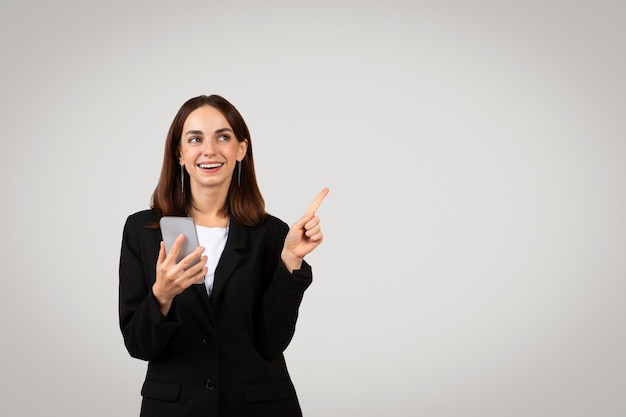 Joyful young businesswoman holding a smartphone and pointing upwards