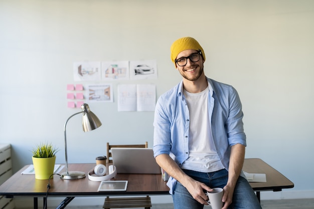 Joyful young casually dressed businessman wearing glasses and standing in a trendy office.