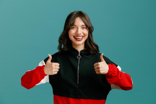 Joyful young caucasian woman looking at camera showing thumbs up isolated on blue background