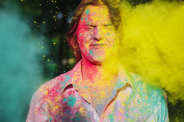 Joyful young caucasian woman playing with yellow and green dry paint at the Holi Festival in the park