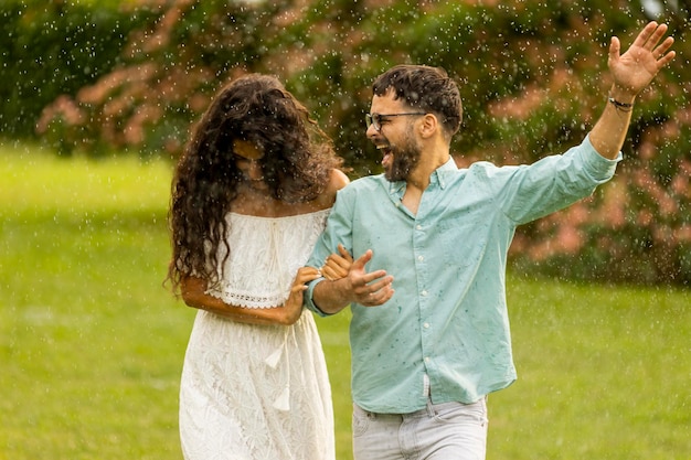 公園で夏の雨に見舞われたうれしそうな若いカップル