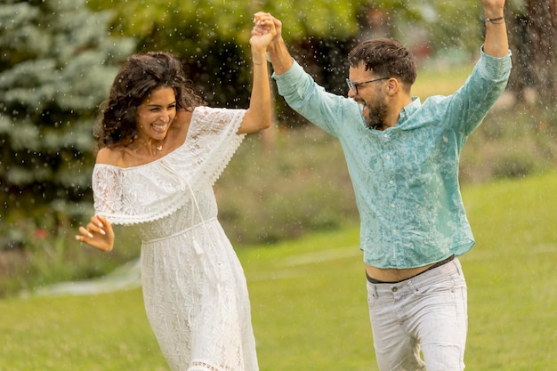 Joyful young couple caught by the summer rain in the park
