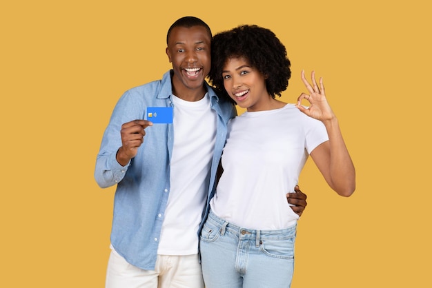 Joyful young couple showcasing a credit card and gesturing an okay sign