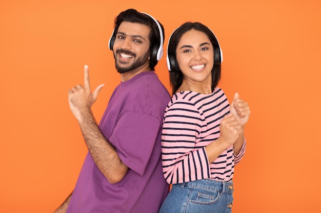 Joyful young eastern couple in wireless headphones listening music