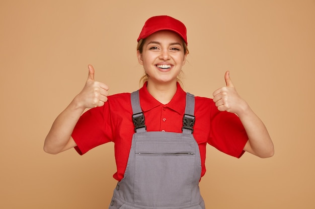 Foto gioioso giovane operaio edile femminile che indossa cappello e uniforme che mostra i pollici in su