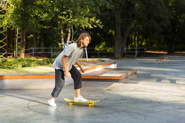 Joyful young guy spending time at the skate park, riding on a skateboard