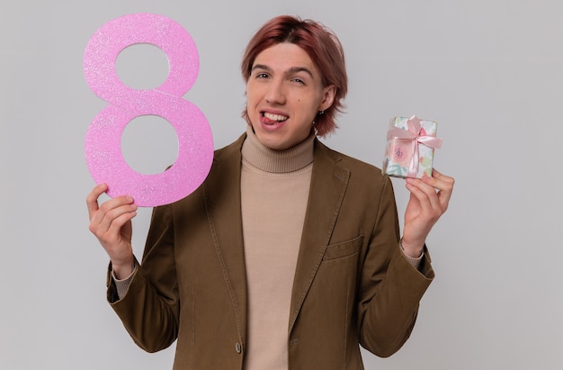 Joyful young handsome man holding pink number eight and gift box 