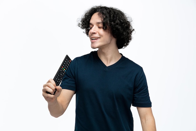 Photo joyful young handsome man holding remote control using it as microphone looking at it singing isolated on white background