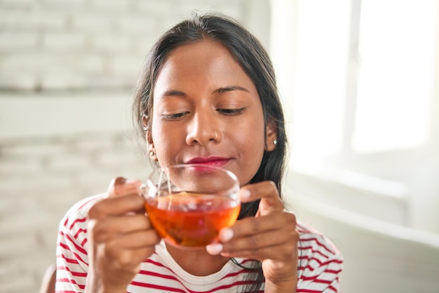 Gioiosa giovane donna indiana gustando una calda tazza di tè