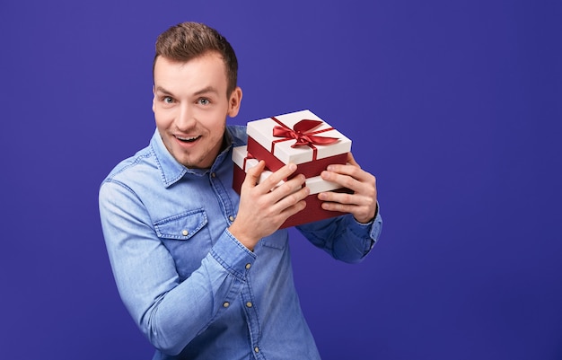 Joyful young man in a blue denim shirt standing with two gifts