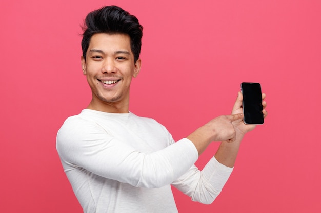 Joyful young man holding and pointing at mobile phone 