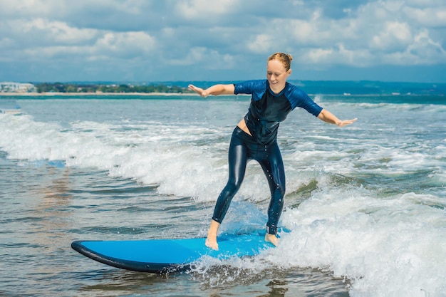 Joyful young woman beginner surfer with blue surf has fun on small sea waves Active family lifestyle people outdoor water sport lesson and swimming activity on surf camp summer vacation