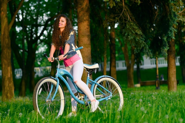일몰 녹색 공원에서 자전거에 즐거운 젊은 여자