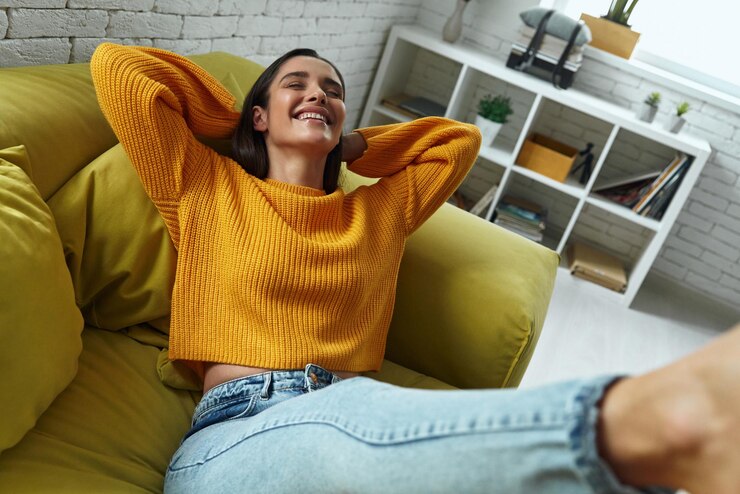 Photo joyful young woman holding hands behind head while sitting on the couch at home