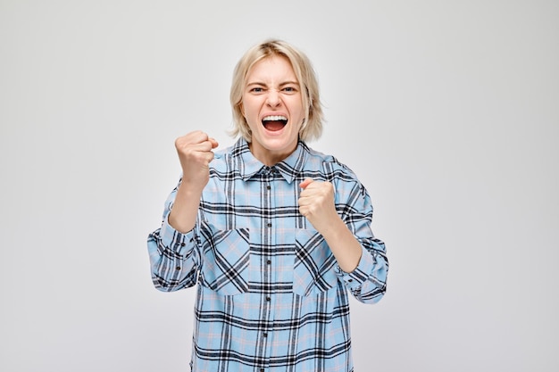 Joyful young woman in plaid shirt celebrating success with fist pump isolated on white background