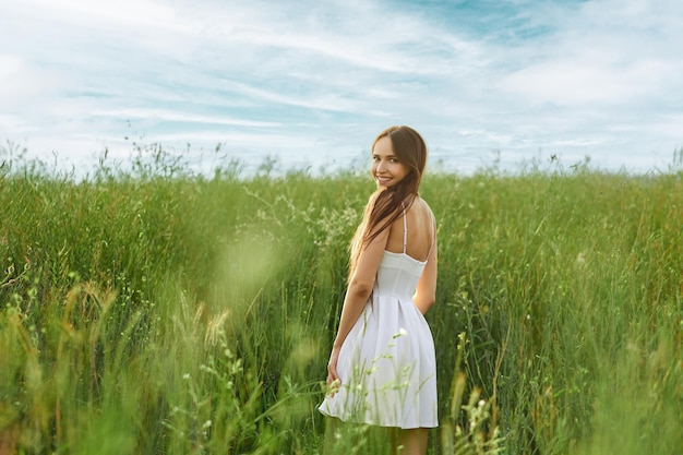 Joyful young woman in sundress in the field turning back