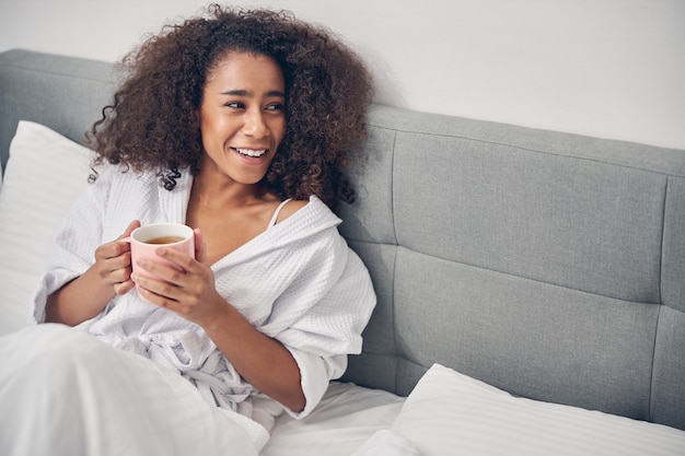 joyous cute young lady with a mug of herbal beverage looking away