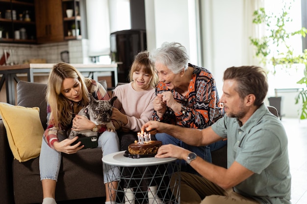 Foto famiglia gioiosa celebra il compleanno di una nonna con una torta in un accogliente soggiorno